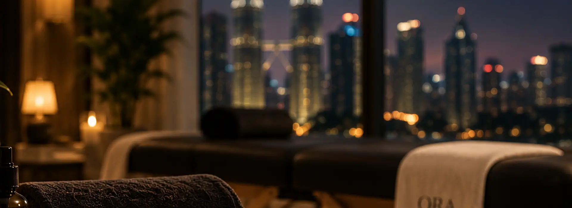 A massage table set up by a window, with the Kuala Lumpur skyline at night
