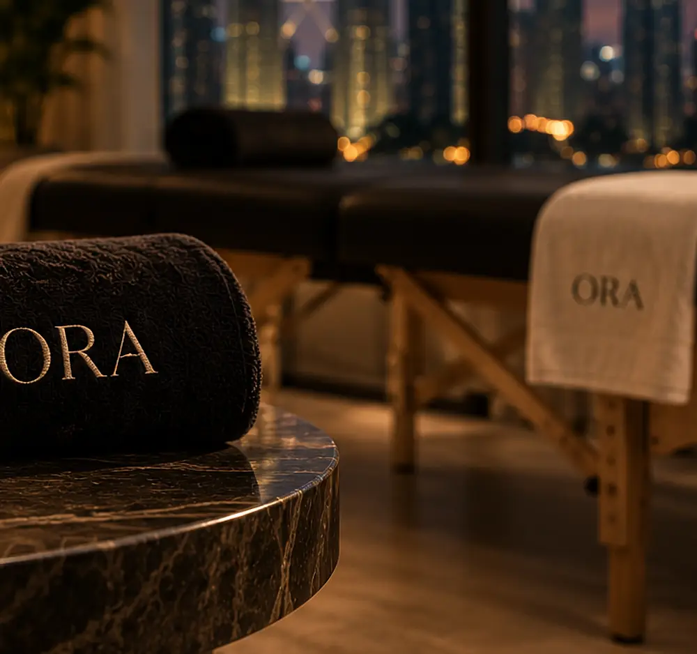 A portable massage table dressed with an ORA towel beside a window